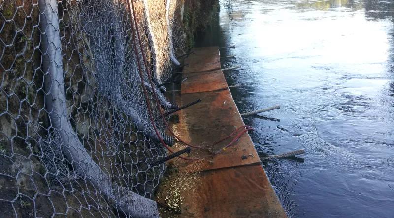 Meshed rock above a rusty platform at river water level